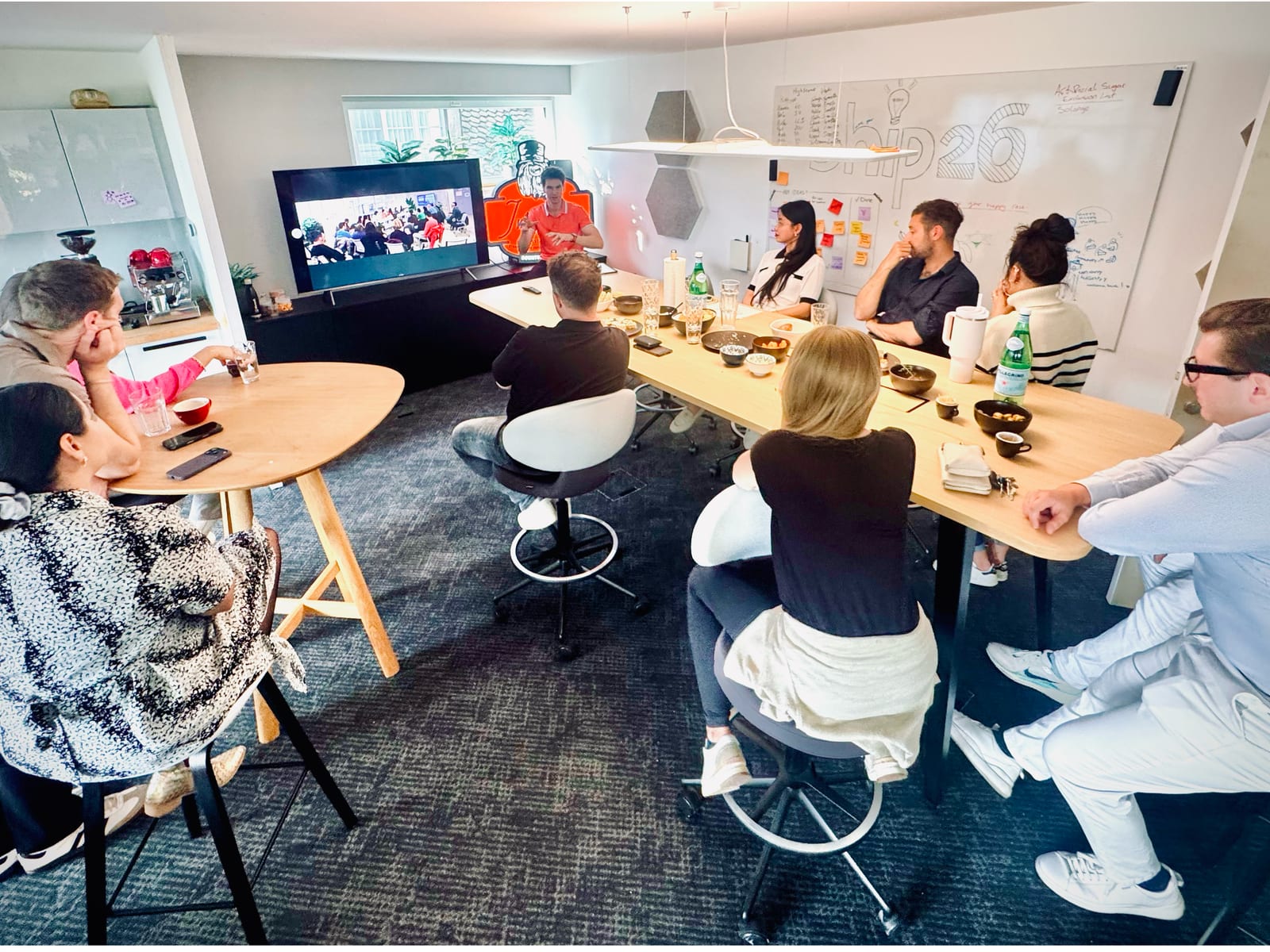 A workshop under way at ship26: people seated around a long table facing a screen, with the ship26 whiteboard behind them